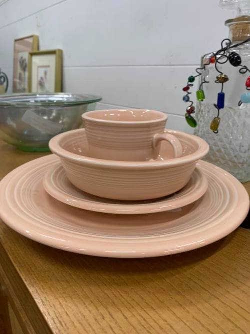 A stack of pastel pink ceramic plates and bowls on a wooden surface, with a decorative glass jar in the background.