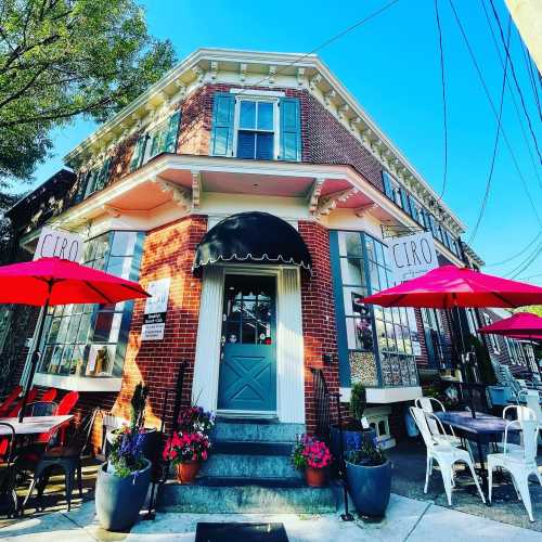 A charming restaurant exterior with a blue door, outdoor seating, and colorful umbrellas on a sunny day.