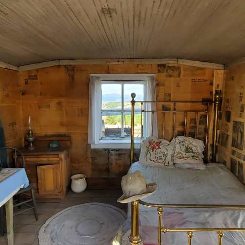 Cozy room with a bed, wooden walls, a window showing a view, and simple furnishings.