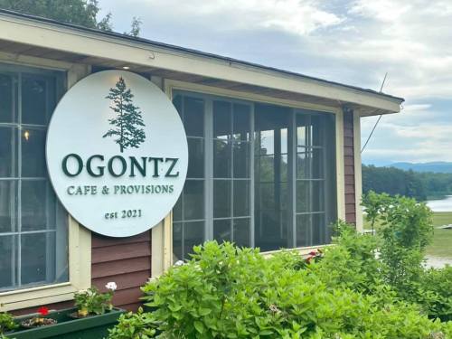 Sign for Ogontz Cafe & Provisions, established 2021, displayed on a building with greenery in the foreground.