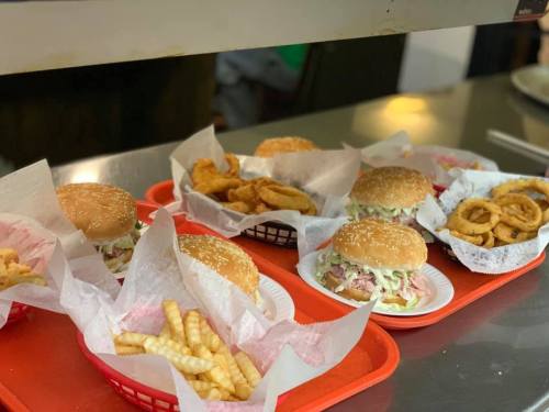 A tray of burgers with sesame seed buns, fries, and onion rings, served in red baskets lined with paper.
