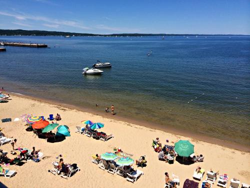 A sunny beach scene with colorful umbrellas, lounge chairs, and boats on calm water under a clear blue sky.