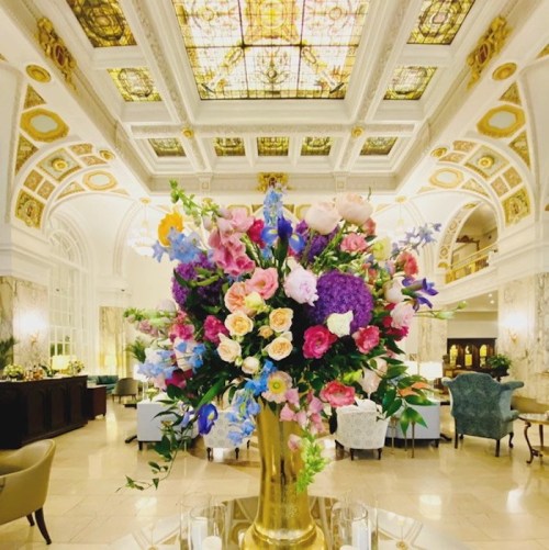 A lavish hotel lobby featuring a large floral arrangement and an ornate ceiling with stained glass.