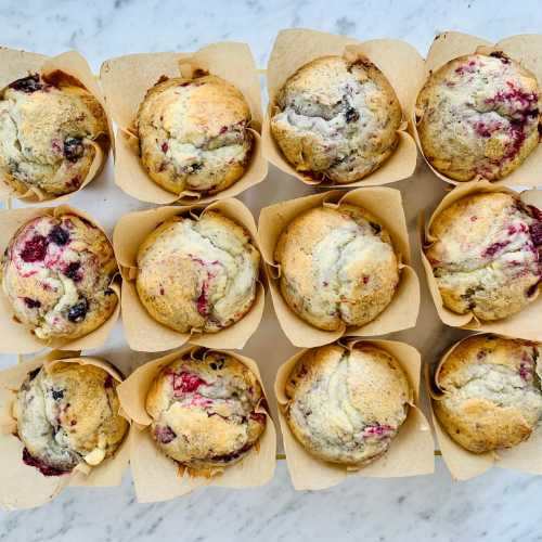 A tray of freshly baked muffins with mixed berries, arranged in paper liners on a marble surface.