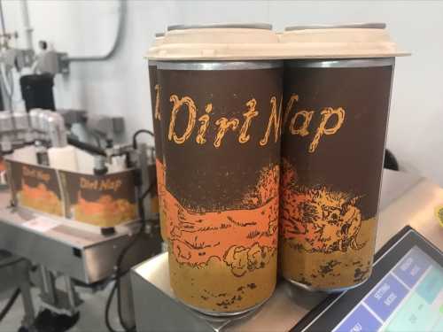 Two cans labeled "Dirt Nap" with a rustic design, placed on a table near a canning machine.