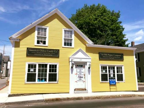 A bright yellow building with white trim, featuring signs for a candy company and a purple company.