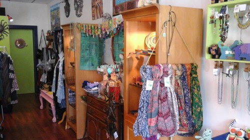 A colorful boutique interior featuring clothing, accessories, and decorative items displayed on wooden shelves.
