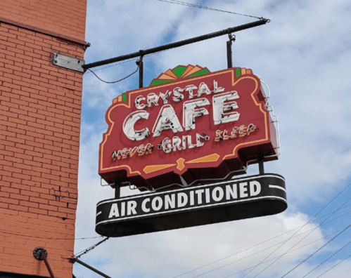 Sign for Crystal Cafe featuring the text "Never Grill, Sleep" and "Air Conditioned" against a blue sky.