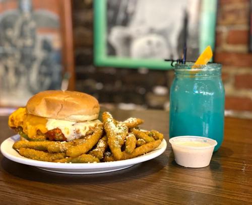 A plate with a sandwich topped with cheese, a side of fries, and a blue drink with an orange slice.