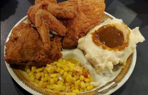 A plate with fried chicken, mashed potatoes with gravy, and a side of corn.