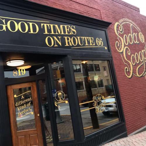 Exterior of a restaurant with a sign reading "Good Times on Route 66" and "Soda" on a brick wall.