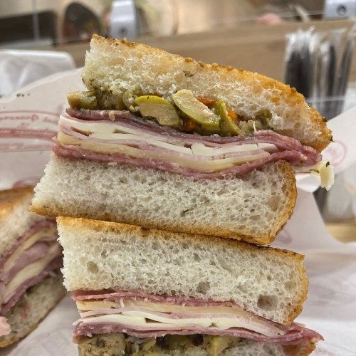 A stacked sandwich with layers of meats, cheese, and pickles on toasted bread, cut in half.