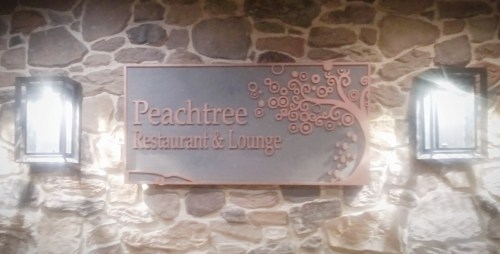 Sign for Peachtree Restaurant & Lounge, mounted on a stone wall, with decorative lighting on either side.