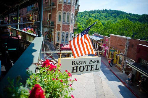 View of Basin Park Hotel sign with an American flag, surrounded by historic buildings and greenery in the background.