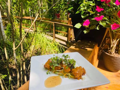 A plate of food with garnishes, set against a lush, green outdoor backdrop with flowers and a wooden walkway.