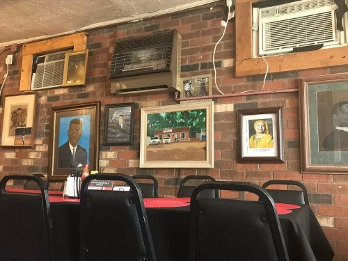 A cozy restaurant interior with a table set for dining, featuring framed portraits and air conditioning units on the wall.