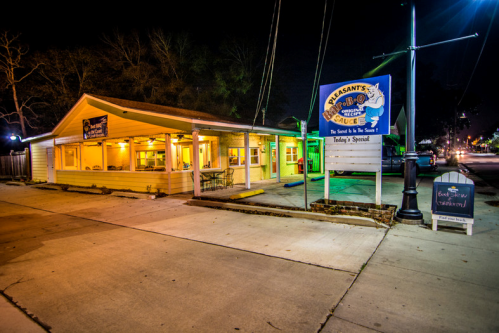 A brightly lit restaurant at night with a sign reading "Pleasant's BBQ Sauce" and a special board outside.