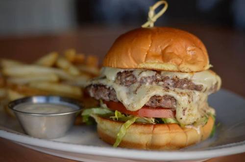 A juicy cheeseburger with lettuce, tomato, and a side of fries on a plate.