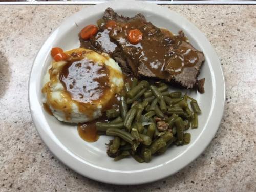 A plate of meatloaf with gravy, mashed potatoes, green beans, and carrots on a beige countertop.