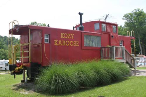 A bright red caboose named "Kozy Kaboose" surrounded by green grass and a wooden deck.
