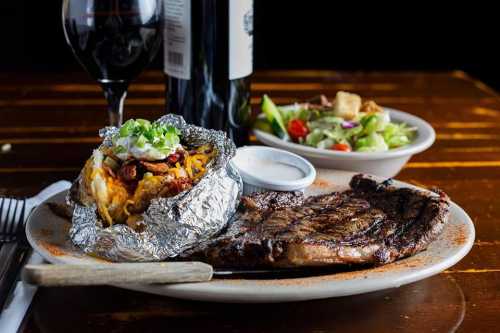 A plate featuring a grilled steak, a baked potato with toppings, a side salad, and a glass of red wine.