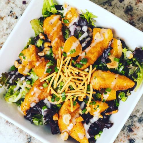 A vibrant salad with mixed greens, crispy chicken, mandarin oranges, cashews, and drizzled with dressing.