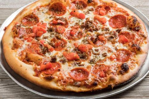 A freshly baked pizza topped with pepperoni, tomatoes, and melted cheese on a silver serving tray.