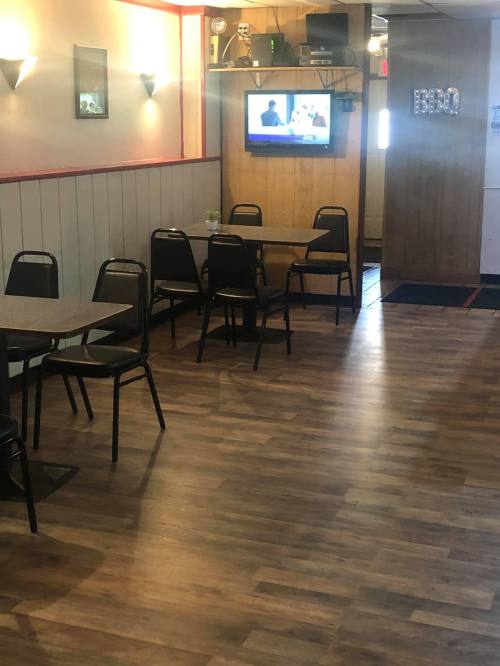 Interior of a restaurant with empty tables and chairs, a TV on the wall, and wooden flooring.