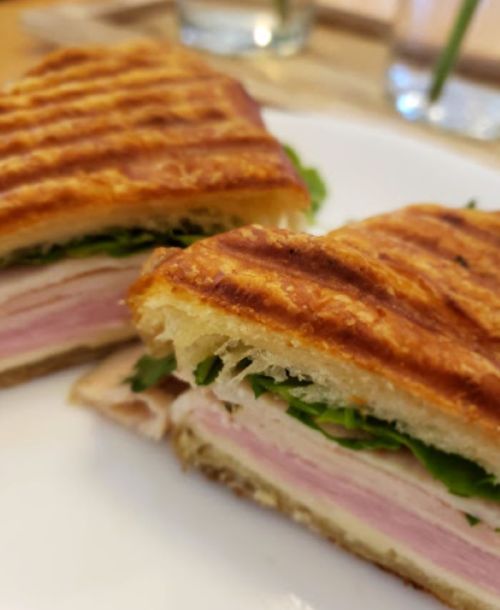 A toasted sandwich filled with layers of ham, cheese, and fresh greens, served on a white plate.