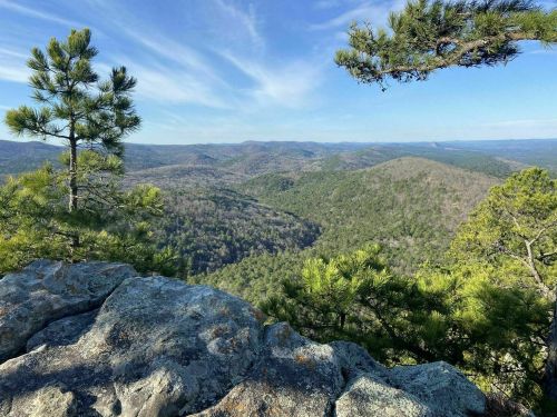 A scenic view from a rocky outcrop, showcasing rolling hills and trees under a clear blue sky.