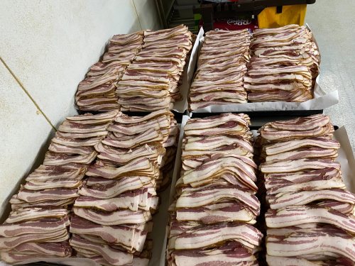 Stacks of neatly arranged bacon strips on trays, ready for cooking or packaging.