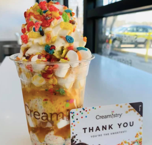A colorful ice cream sundae topped with whipped cream and cereal, next to a "Thank You" card from Creamistry.
