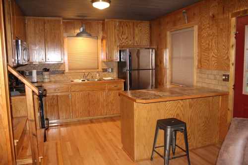 Cozy wooden kitchen with cabinets, a countertop, and stainless steel appliances, featuring a small bar stool.