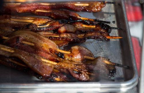 Grilled skewers of bacon with a crispy texture, arranged on a metal tray.