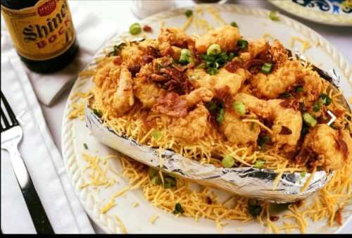 A loaded baked potato topped with fried shrimp, bacon, green onions, and shredded cheese, served on a plate.