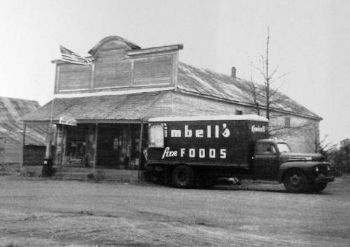 A vintage black-and-white photo of a store with a delivery truck parked outside, featuring the sign "Imbell's Fine Foods."