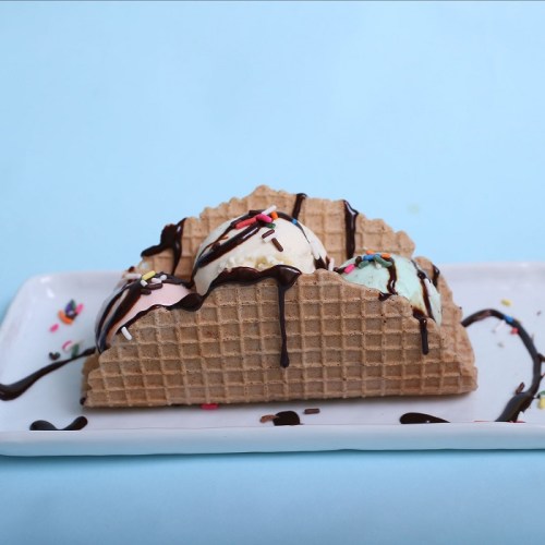A waffle cone filled with three scoops of ice cream, drizzled with chocolate and topped with colorful sprinkles.