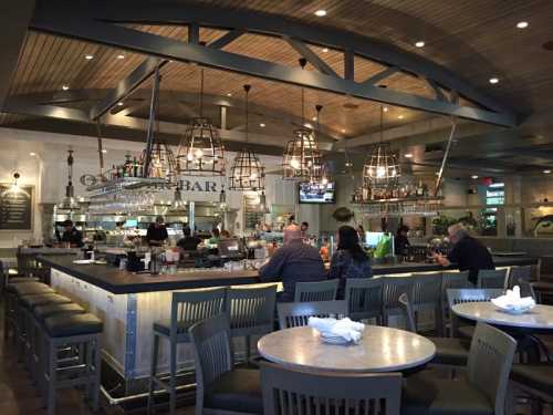 A modern bar and dining area with pendant lights, high stools, and patrons enjoying drinks and meals.