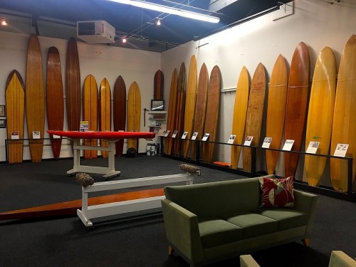 A room displaying vintage surfboards on the walls, with a green couch and informational plaques in front.