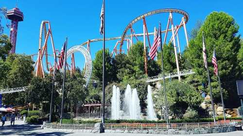 A vibrant amusement park scene featuring roller coasters, fountains, and flags under a clear blue sky.