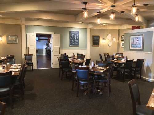 Interior of a restaurant featuring wooden tables, black chairs, and warm lighting, with a cozy, inviting atmosphere.