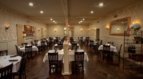 Elegant restaurant interior with white tablecloths, wooden chairs, and soft lighting, creating a cozy atmosphere.