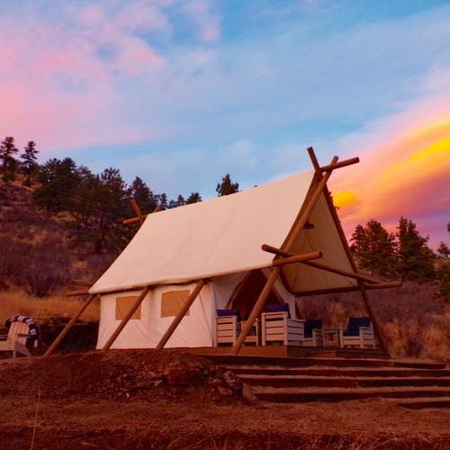 A canvas tent on a hillside at sunset, surrounded by trees and colorful sky.