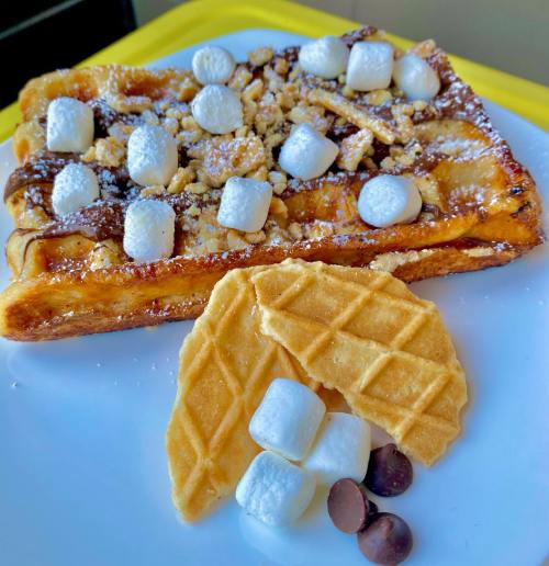 A plate of waffles topped with marshmallows, chocolate chips, and crushed nuts, alongside two waffle cookies.