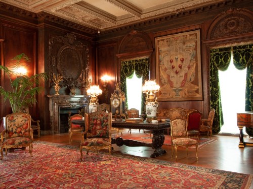 Luxurious room with ornate furniture, rich wood paneling, a large rug, and elegant drapes, featuring a decorative fireplace.