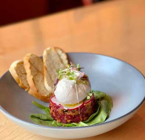 A plate with a colorful dish featuring a poached egg on a bed of greens, accompanied by slices of toasted bread.