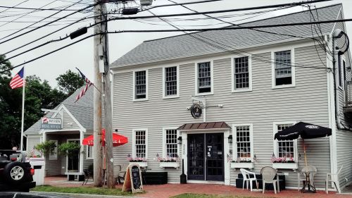 A gray building with multiple windows, featuring outdoor seating and flags, surrounded by power lines.