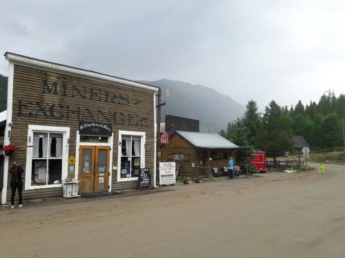 Historic buildings in a small mountain town, with a cloudy sky and trees in the background.