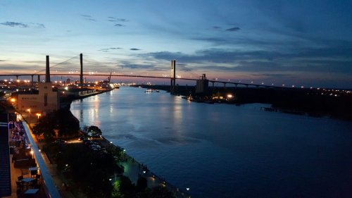 A serene river scene at dusk, with a bridge and city lights reflecting on the water under a colorful sky.