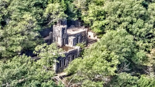 Aerial view of a stone ruin surrounded by dense green trees, hinting at a historical structure in nature.